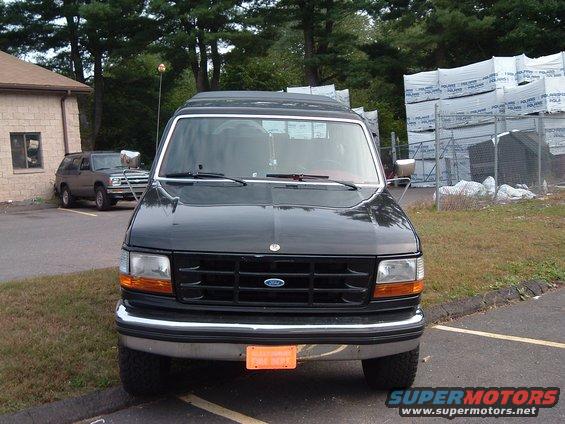 Front view of a black Ford truck, parked next to another SUV. Stacks of materials are behind a fence