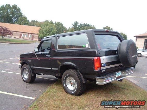 Black Ford Bronco, rear 3/4 view, with spare tire mounted on rear door. Red pinstripe along the body