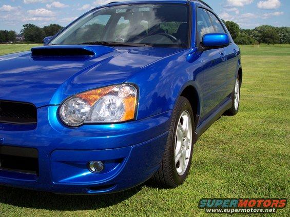 Blue Subaru Impreza wagon parked on grass, front quarter view. Hood scoop visible