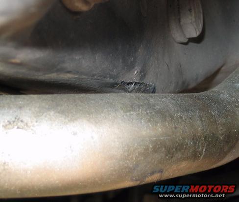 Close-up of exhaust pipe with undercarriage detail. SUPERMOTORS.NET logo visible