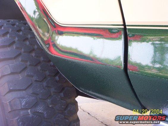 Close-up of a dark green lower body panel and a large tire with aggressive tread
