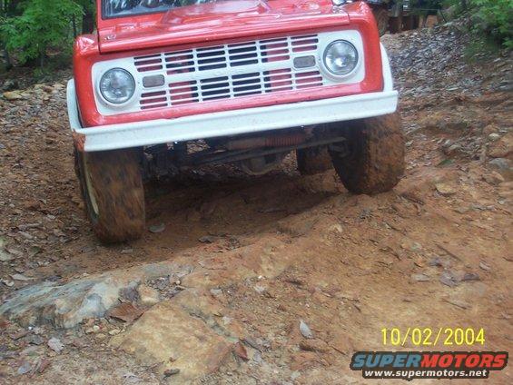 Red off-road vehicle with white bumper and grille, front view, on a dirt trail
