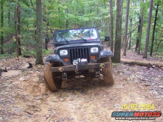 Black 1994 Jeep YJ on a muddy forest trail, front view