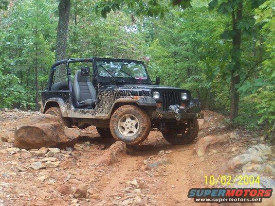 Black Jeep Wrangler on a muddy, rocky trail, front winch visible