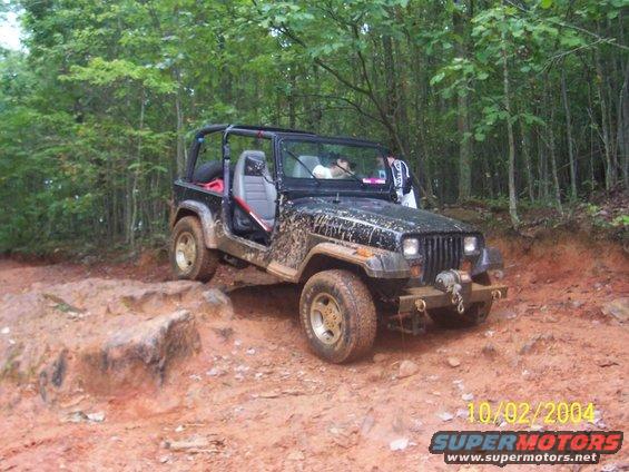 1994 Jeep YJ on a muddy, rocky trail with trees in the background