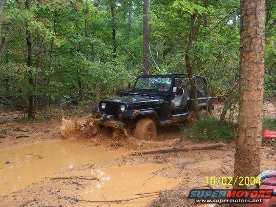 black Jeep Wrangler driving through mud on a wooded trail