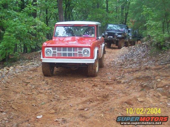 Red Ford Bronco driving on a dirt trail with a black Jeep following behind