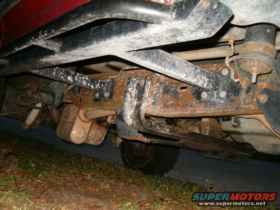Undercarriage of a red vehicle with significant rust on the frame and exhaust system