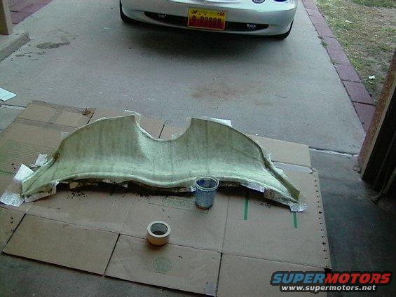 Fiberglass car stereo component on cardboard with tape and a cup. Car bumper visible in background
