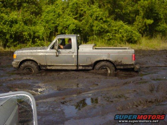 Silver Ford pickup truck stuck deep in mud with trees in background