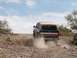 1990 Ford Bronco - A 1990 Ford Bronco navigates a dusty, off-road trail under a partly cloudy sky.