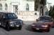 2000 Ford Crown Victoria - A maroon 2000 Ford Crown Victoria is parked in front of a large building, alongside a black SUV.