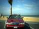2000 Ford Crown Victoria - A red 2000 Ford Crown Victoria is parked facing the ocean on a sunny day, with a palm tree to its left.