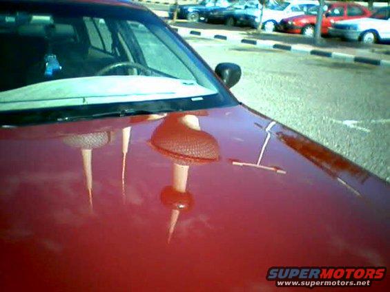 Red car hood reflecting a tower and other vehicles parked in the background