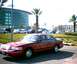 2000 Ford Crown Victoria - A red 2000 Ford Crown Victoria is parked in a lot with other vehicles and a modern building in the background.