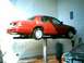 2000 Ford Crown Victoria - A red sedan is elevated on a hydraulic lift, with another vehicle partially visible beneath it.