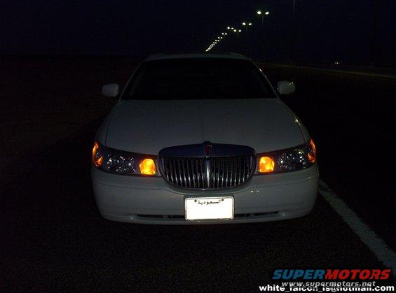White sedan with chrome grille and amber turn signals, front view at night