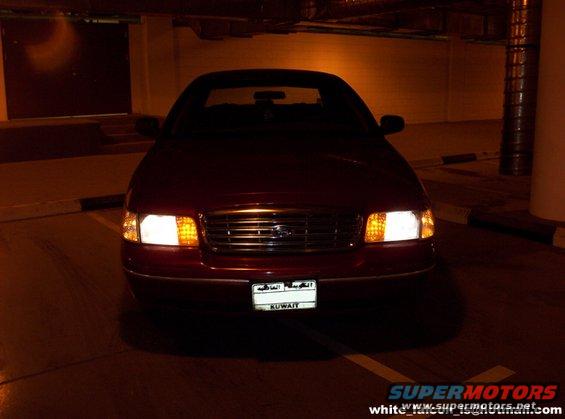 Red 2000 Ford Crown Victoria front view with headlights on