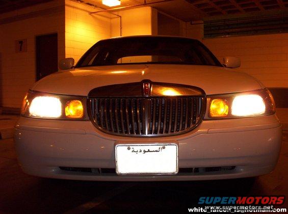 White Lincoln Town Car front view, grille with chrome accents, illuminated headlights and amber turn signals, Saudi Arabian license plate
