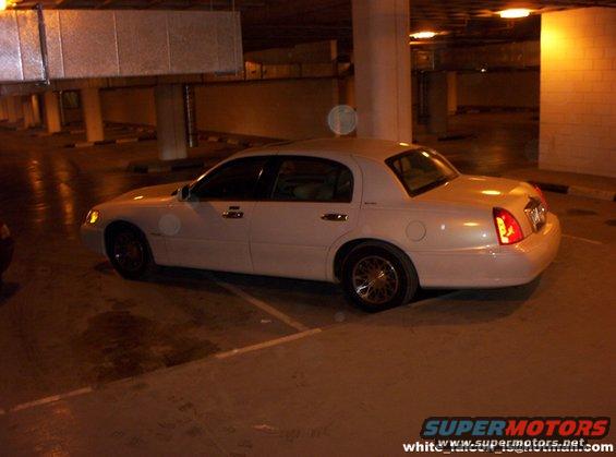 White sedan parked in a garage, side view. The car appears to be a Lincoln Town Car