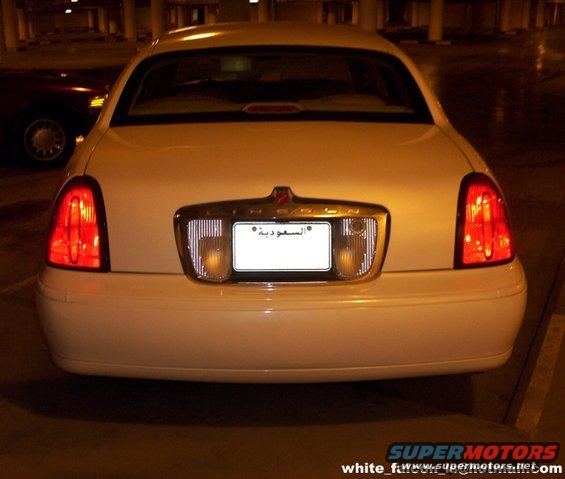 Rear view of a white 2000 Ford Crown Victoria parked in a garage. Another dark car is visible to the left
