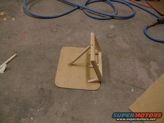 Wooden jig on concrete floor with blue hoses in background