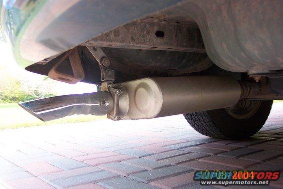 Underside view of a car's exhaust pipe and muffler, with a tire visible