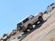 1988 Ford Bronco - Two white Ford Broncos ascend a challenging off-road trail under a clear blue sky.