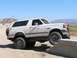 1988 Ford Bronco - A white Ford Bronco navigates an off-road obstacle course on a sunny day.