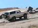 1988 Ford Bronco - A white 1988 Ford Bronco navigates a rocky off-road course under a clear blue sky.