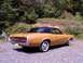 1970 Mercury Cougar - A gold 1970 Mercury Cougar with a black vinyl roof is parked on a gravel surface with trees in the background.