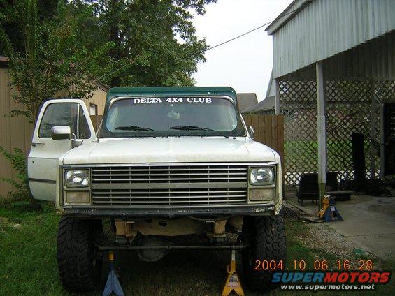White pickup truck with green top, lifted suspension, and "DELTA 4X4 CLUB" sticker on windshield
