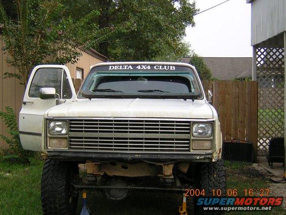 Front view of a white lifted pickup truck with the driver's door open. It has a 'DELTA 4X4 CLUB' sticker on the windshield