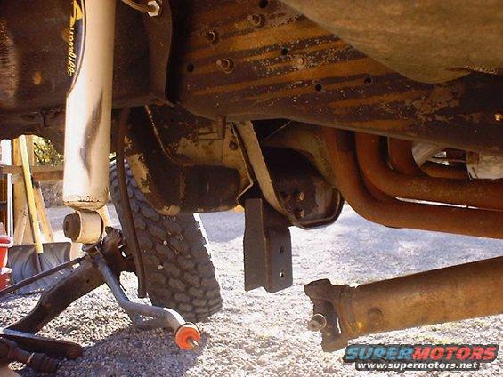 Vehicle undercarriage with suspension parts removed, showing rusty exhaust pipes and driveshaft