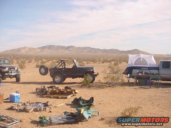 Two Jeeps and a pickup truck with a rooftop tent are parked in a desert campsite