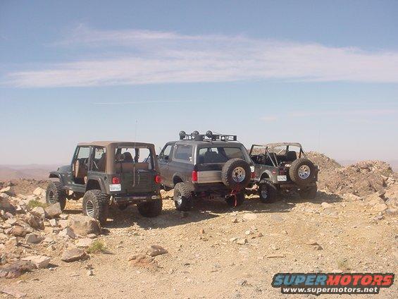 1988 Ford Bronco parked with two Jeeps on a rocky desert hill under a blue sky