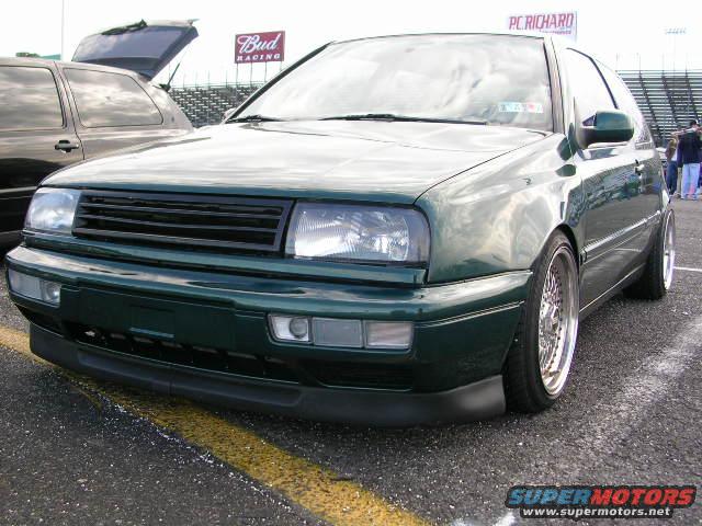 Green hatchback with black grille and aftermarket wheels parked next to a dark SUV