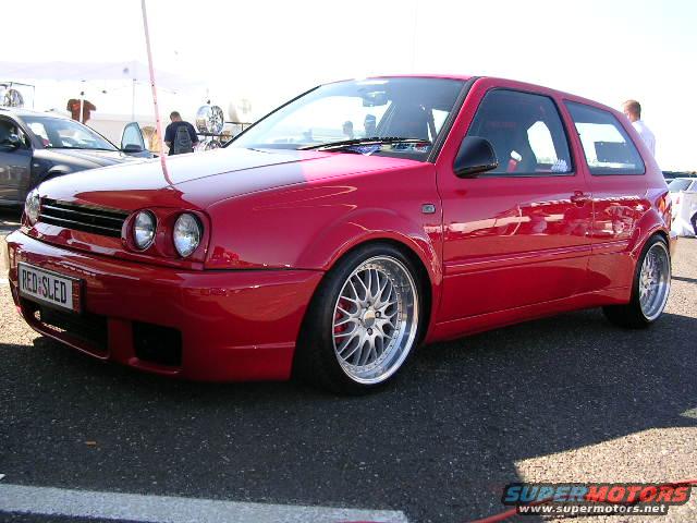 Red VW Golf GTI with custom wheels and a license plate that says 'RED-SLED'