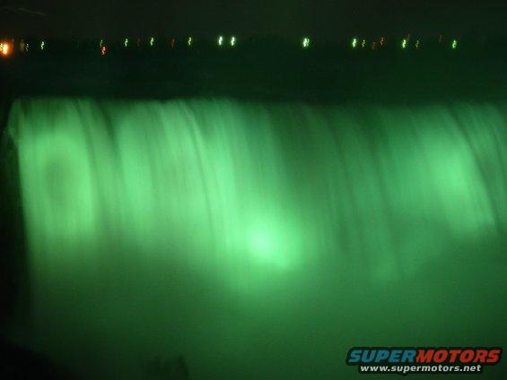 Niagara Falls illuminated green at night with lights visible in the distance
