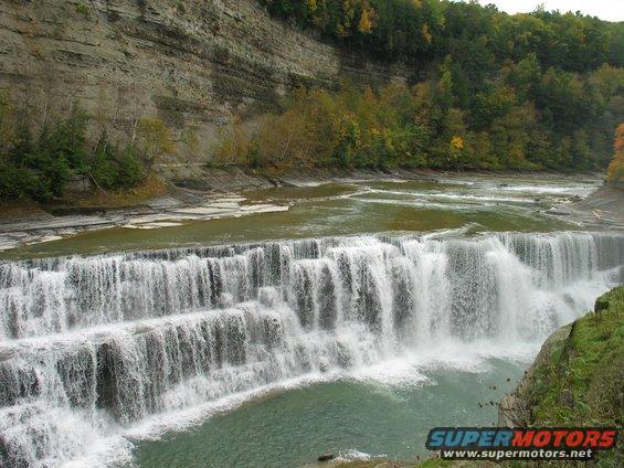 Wide waterfall cascading over layered rocks with trees on the cliffside