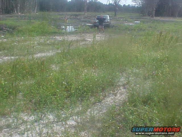 1992 Ford Bronco parked in a muddy field with trees in the background