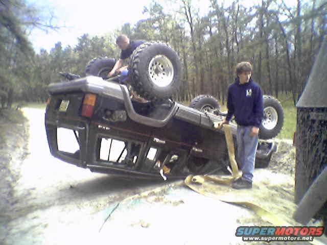 SUV flipped on its side with two guys nearby, one on top, one holding a strap