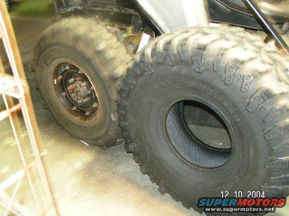 Two large off-road tires, one mounted on a rim, the other loose, indoors