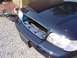 1999 Ford Crown Victoria - The front grille of a dark blue Ford Crown Victoria has been removed, with the grille assembly lying on the ground nearby.