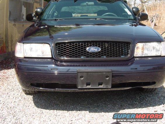 Front view of a dark-colored Ford Crown Victoria with a honeycomb grille and a license plate bracket
