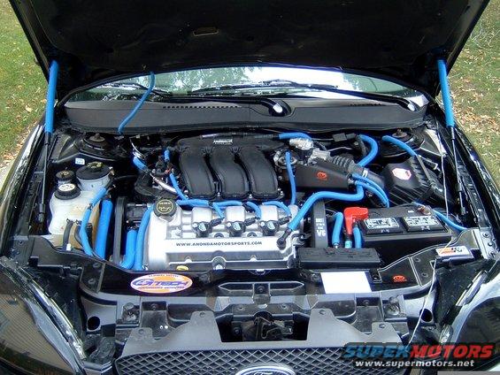 Engine bay of a car with blue hoses and wiring, showing the engine block, battery, and air intake