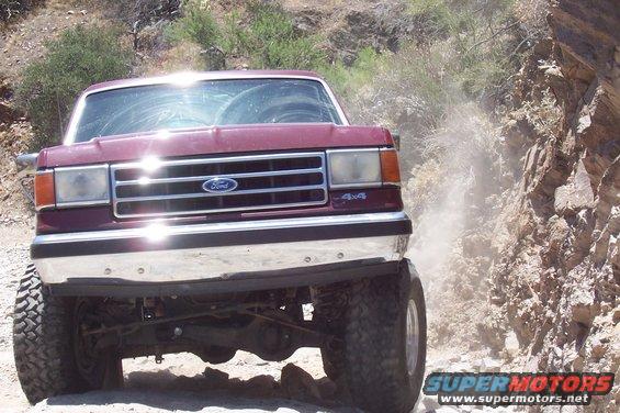 Maroon Ford Bronco driving on a dusty dirt road with rocky hillsides