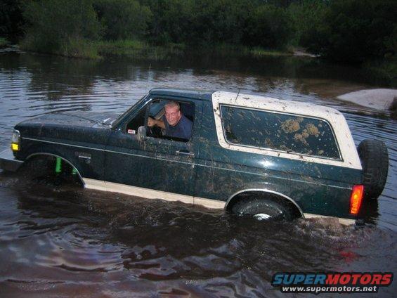 1992 Ford Bronco driving through murky water, mud splattered on windows
