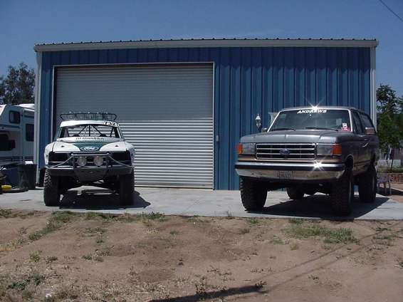 Ford Bronco and a race truck parked in front of a blue garage
