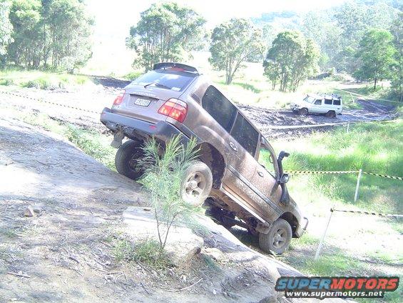 Brown SUV attempting to climb a steep, muddy incline with another white SUV in the background